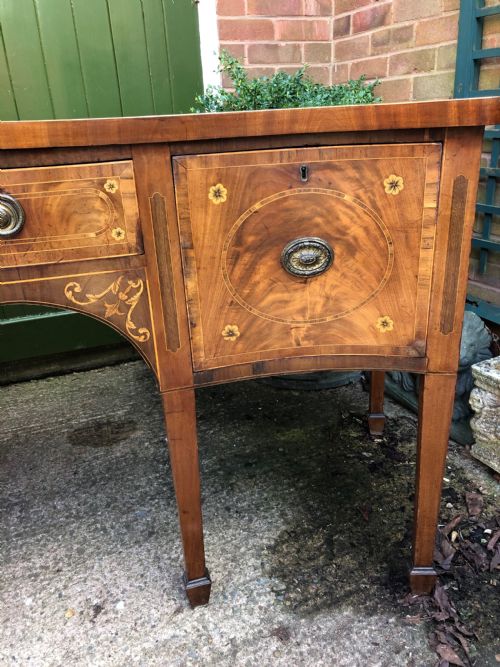 fig 4. A late 18th-century George III mahogany sideboard featuring a serpentine front, floral marquetry inlay, tapering square legs with spade feet, and brass oval handles.
