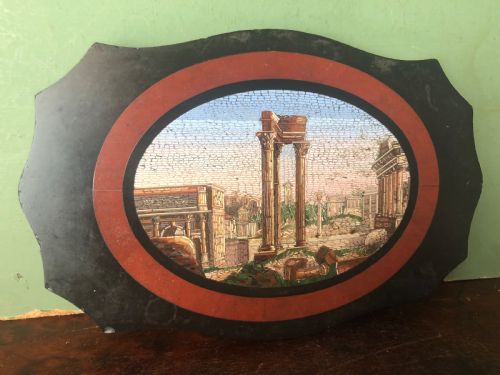 fig 1. A cartouche-shaped black marble paperweight with a terracotta-coloured inlay ring surrounding a central oval micro-mosaic depicting classical Roman architectural ruins.