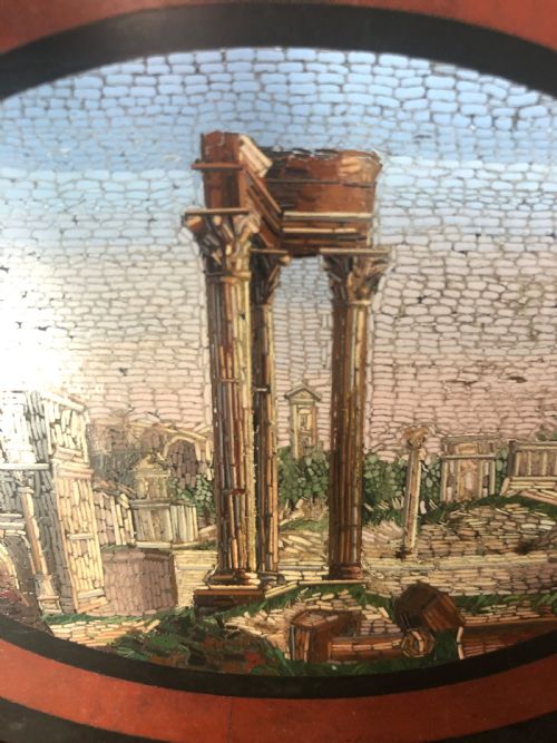 fig 2. A cartouche-shaped black marble paperweight with a terracotta-coloured inlay ring surrounding a central oval micro-mosaic depicting classical Roman architectural ruins.