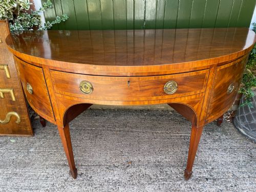 fig 1. A late 18th-century George III mahogany demi-lune sideboard featuring inlaid stringing, a central drawer, curved side doors, and tapered square legs.