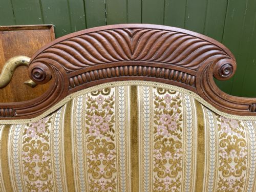fig 2. An early nineteenth-century Regency mahogany sofa featuring double scroll-ended arms, a carved crest rail, striped gold velvet upholstery, matching bolster cushions, and turned legs on brass castors.
