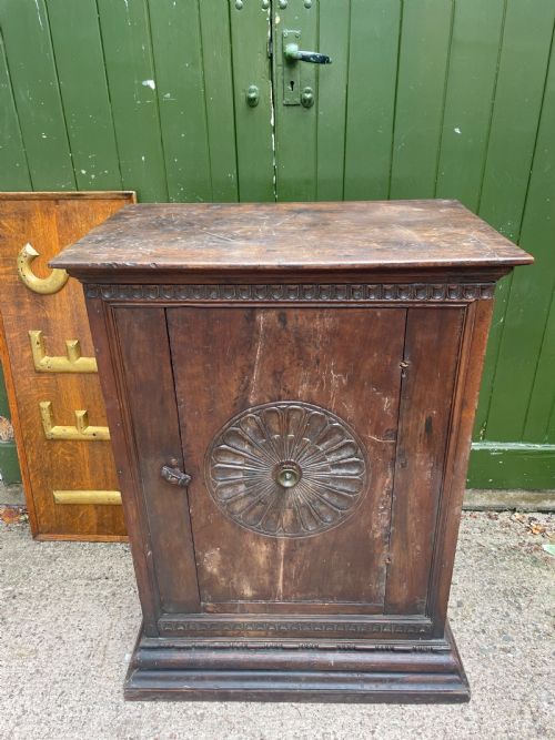 fig 1. An early 18th-century Italian Tuscan walnut pedestal cupboard featuring a single cupboard door carved with a central circular rosette motif and framed by architectural moulding on a plinth base.
