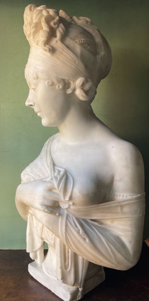 fig 2. A late nineteenth-century carved white statuary marble portrait bust depicting a female figure with draped cloth held across her chest and stylized hair.