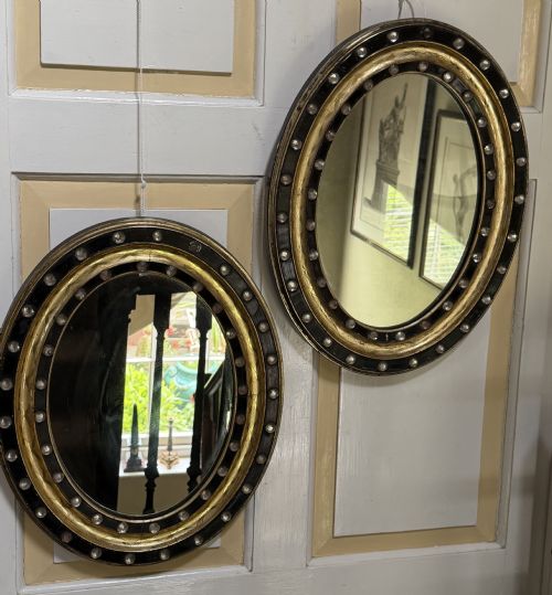 Scarce Pair of Early C19th Irish Oval Ebonised , Parcel-gilt and Glass Cabochon Mounted Mirrors of Smaller Scale .