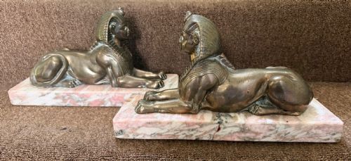 fig 1. A pair of bronze recumbent sphinx sculptures featuring detailed Nemes headdresses mounted on rectangular pink marble bases.