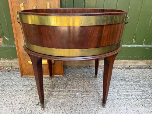 fig 1. An 18th-century George III mahogany oval wine cooler with thick brass bands and brass handles, resting on a four-legged tapered stand with castors.