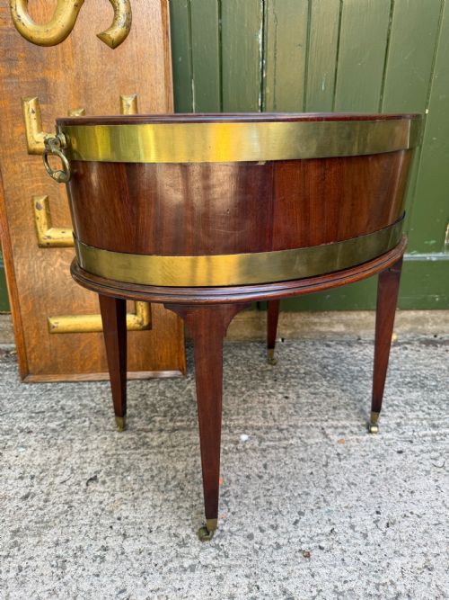fig 2. An 18th-century George III mahogany oval wine cooler with thick brass bands and brass handles, resting on a four-legged tapered stand with castors.