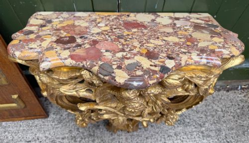 fig 1. An 18th-century style French carved giltwood wall console table featuring intricate foliage, a central bird motif, and a variegated pink and ochre Breche dAlep marble top.
