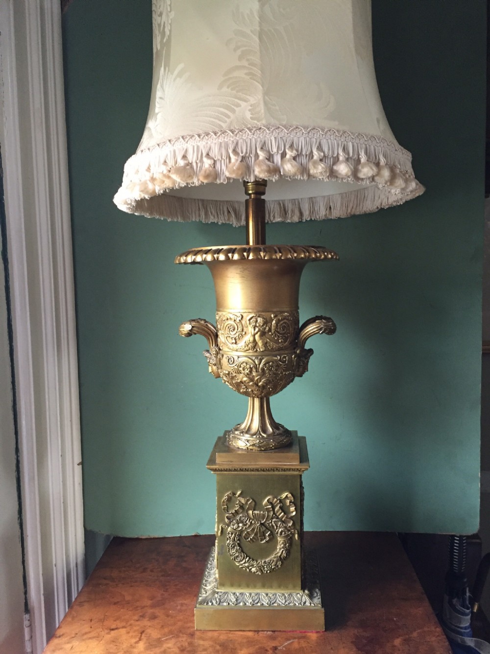 Late 19th-century gilded bronze Empire style table lamp featuring a classical urn base with relief work and a fringed shade.