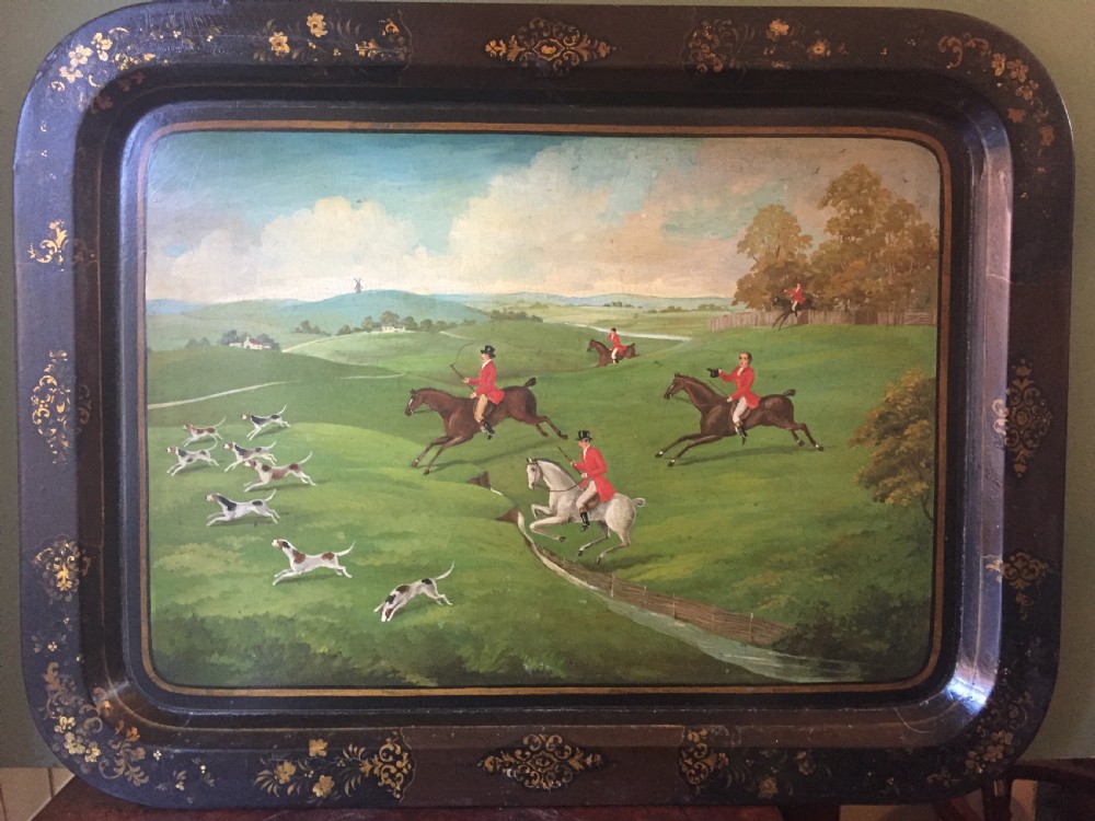 An early 19th-century rectangular papier-mache tray featuring a gilded scrollwork border and a central hand-painted scene of horsemen and hounds engaged in a fox hunt across a countryside landscape. View II