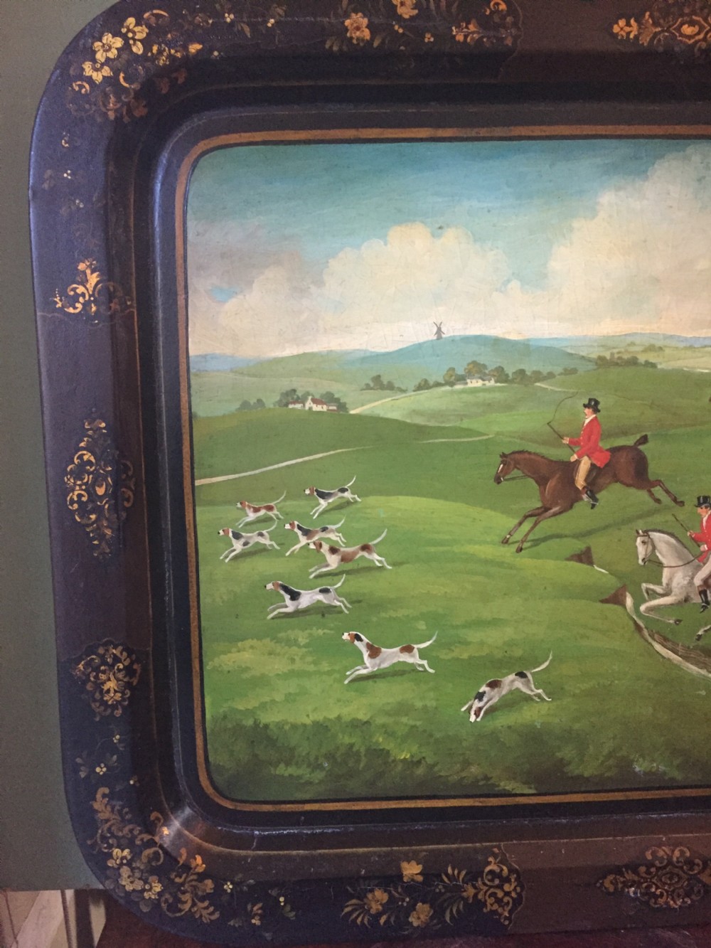 An early 19th-century rectangular papier-mache tray featuring a gilded scrollwork border and a central hand-painted scene of horsemen and hounds engaged in a fox hunt across a countryside landscape. View IV