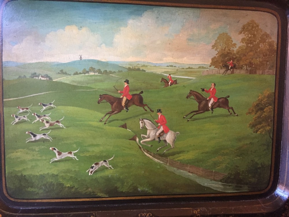 An early 19th-century rectangular papier-mache tray featuring a gilded scrollwork border and a central hand-painted scene of horsemen and hounds engaged in a fox hunt across a countryside landscape. View XII