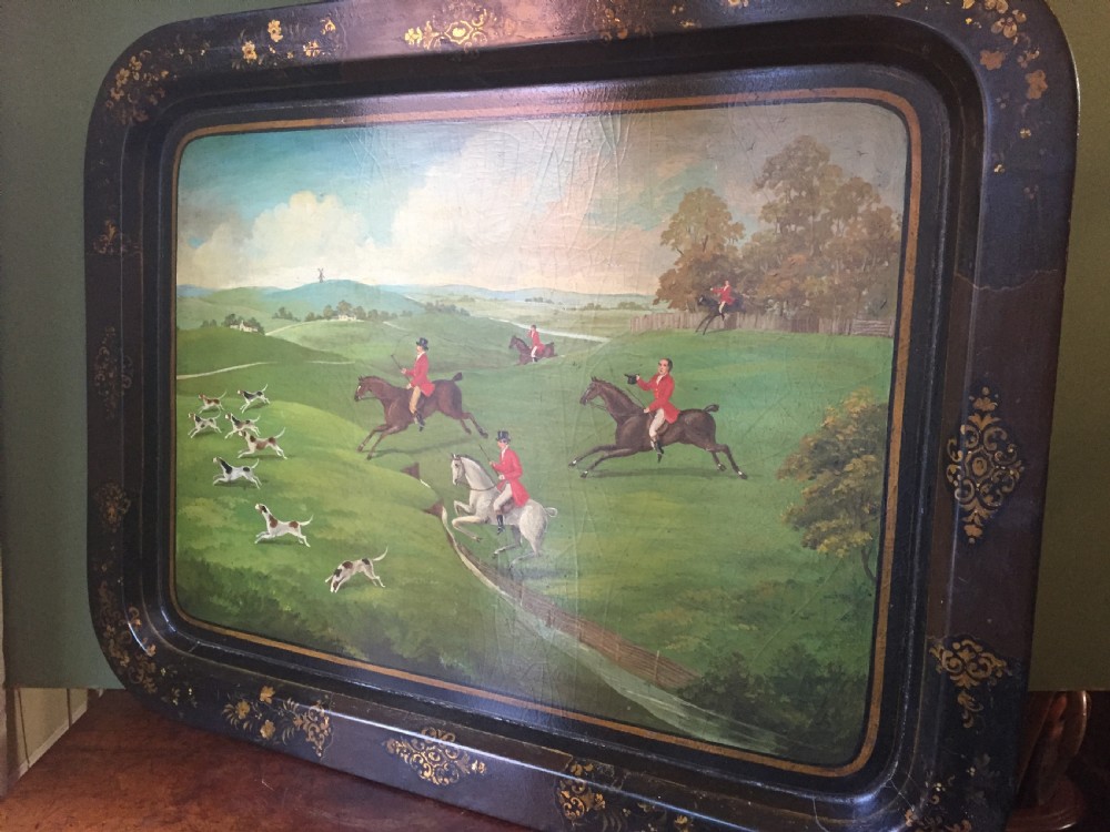 An early 19th-century rectangular papier-mache tray featuring a gilded scrollwork border and a central hand-painted scene of horsemen and hounds engaged in a fox hunt across a countryside landscape. View XVI