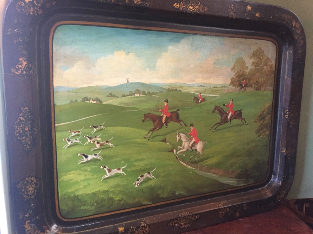 An early 19th-century rectangular papier-mache tray featuring a gilded scrollwork border and a central hand-painted scene of horsemen and hounds engaged in a fox hunt across a countryside landscape. View XVII