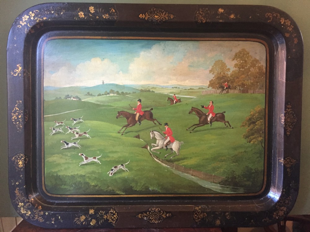 An early 19th-century rectangular papier-mache tray featuring a gilded scrollwork border and a central hand-painted scene of horsemen and hounds engaged in a fox hunt across a countryside landscape. View XIX