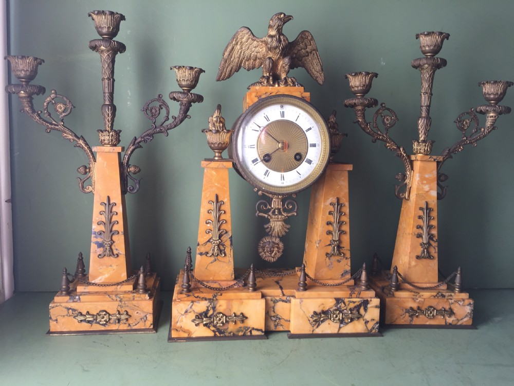A late nineteenth-century French Empire style clock garniture crafted from yellow Siena marble and gilt ormolu, featuring a central clock topped with an eagle and flanked by two candelabra.