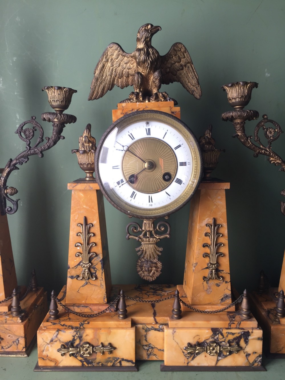 A late nineteenth-century French Empire style clock garniture crafted from yellow Siena marble and gilt ormolu, featuring a central clock topped with an eagle and flanked by two candelabra. View V