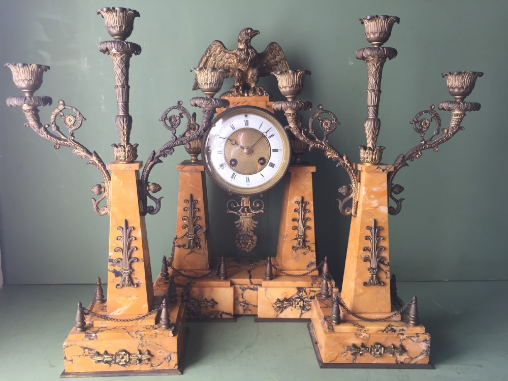 A late nineteenth-century French Empire style clock garniture crafted from yellow Siena marble and gilt ormolu, featuring a central clock topped with an eagle and flanked by two candelabra. View XXVIII