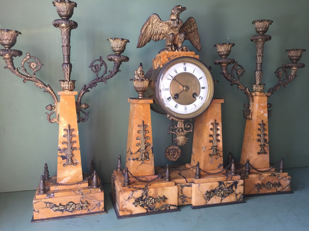 A late nineteenth-century French Empire style clock garniture crafted from yellow Siena marble and gilt ormolu, featuring a central clock topped with an eagle and flanked by two candelabra. View XXX