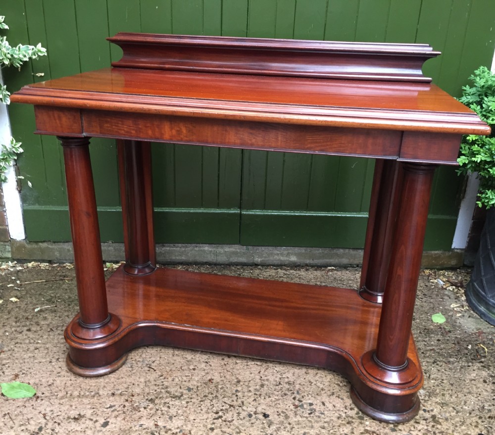 A William IV mahogany hall console table with cylindrical column supports, a raised rear gallery, and a lower plinth shelf.