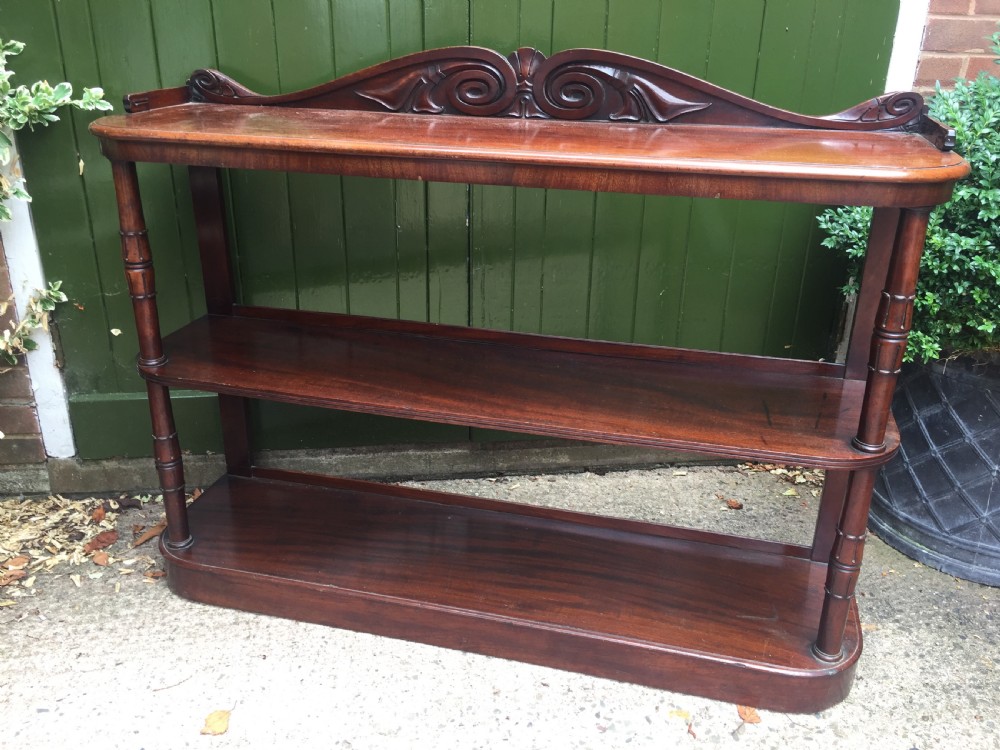An early 19th-century George IV three-tier mahogany buffet featuring a carved scroll backboard, turned column supports, and a solid plinth base.