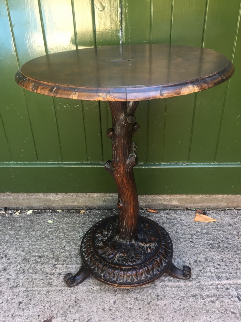 A late nineteenth-century dark brown linden wood side table featuring a circular top supported by a carved tree-trunk stem and a foliage-adorned tripod base.