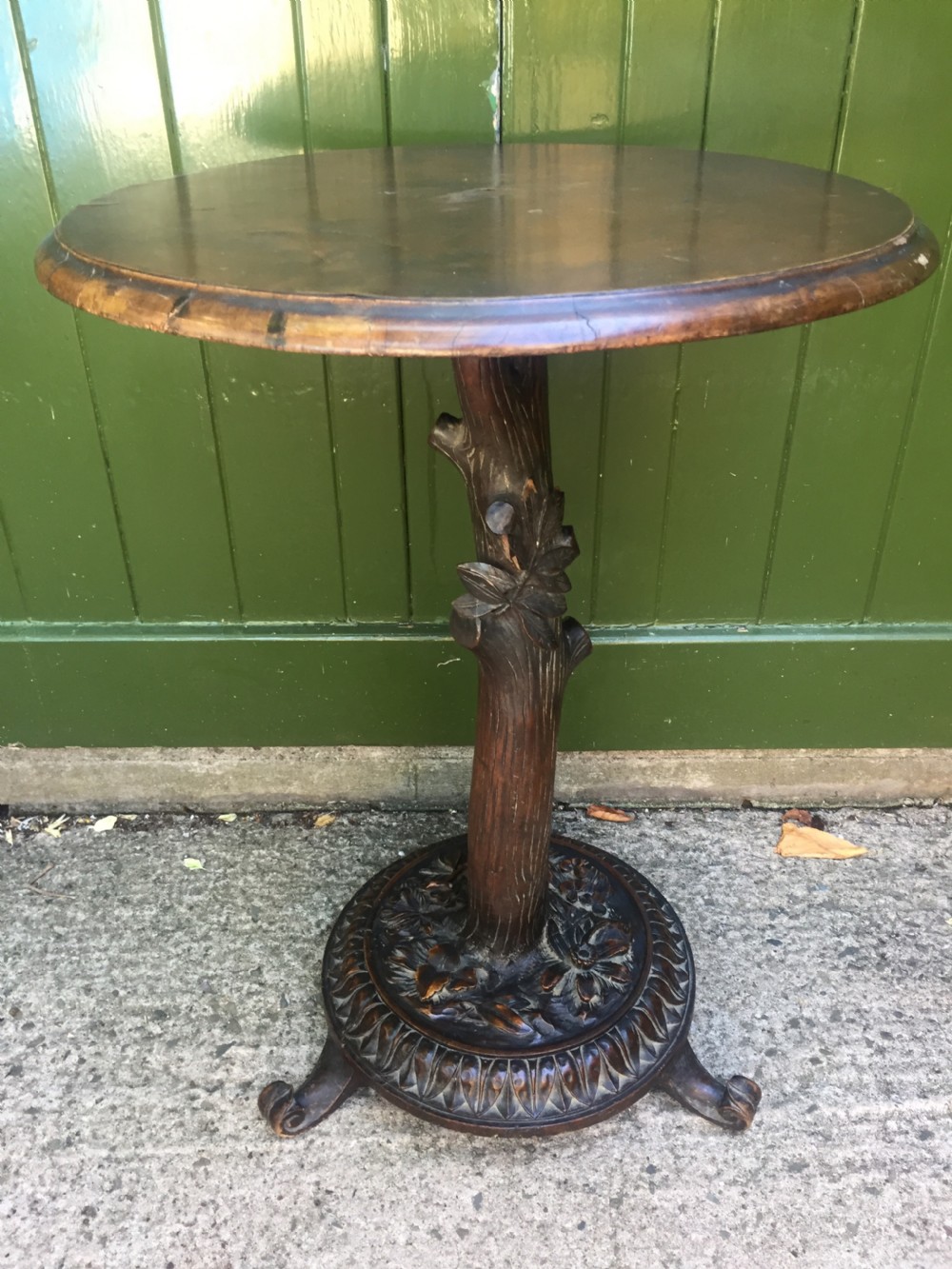 A late nineteenth-century dark brown linden wood side table featuring a circular top supported by a carved tree-trunk stem and a foliage-adorned tripod base. View X
