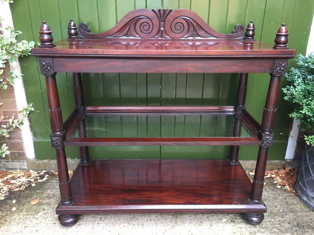 A George IV mahogany three-tier buffet featuring a carved scroll upstand, turned finials, column supports, and a glass-inset middle shelf. View XI