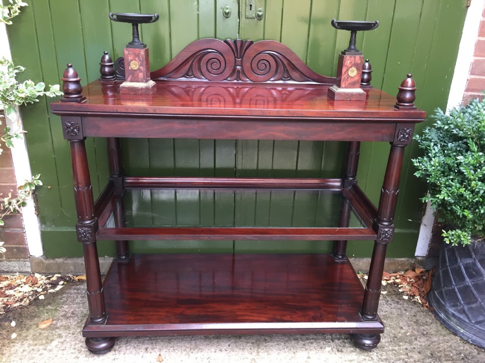 A George IV mahogany three-tier buffet featuring a carved scroll upstand, turned finials, column supports, and a glass-inset middle shelf. View XVII