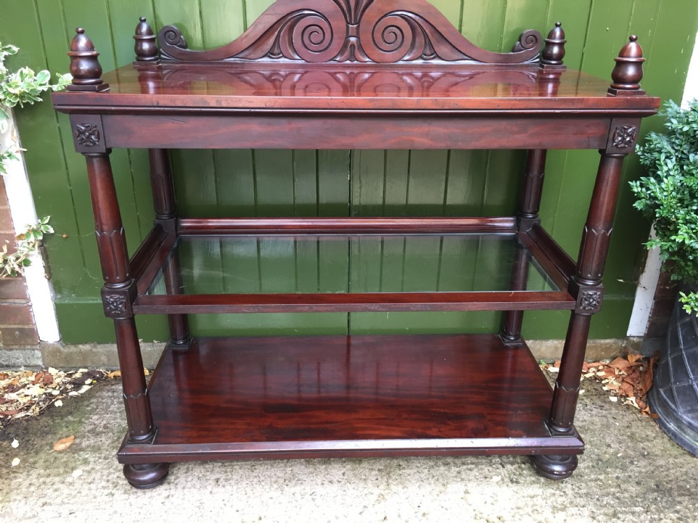 A George IV mahogany three-tier buffet featuring a carved scroll upstand, turned finials, column supports, and a glass-inset middle shelf. View V