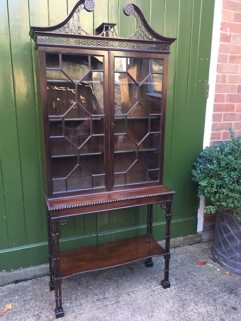 A late 19th-century Chippendale Revival mahogany glazed cabinet on stand featuring a swan-neck pediment, fretwork frieze, astragal glass doors, and turned legs with a lower shelf. View II