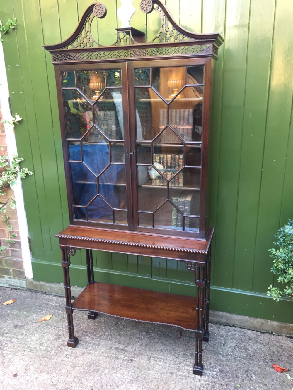 A late 19th-century Chippendale Revival mahogany glazed cabinet on stand featuring a swan-neck pediment, fretwork frieze, astragal glass doors, and turned legs with a lower shelf. View XV