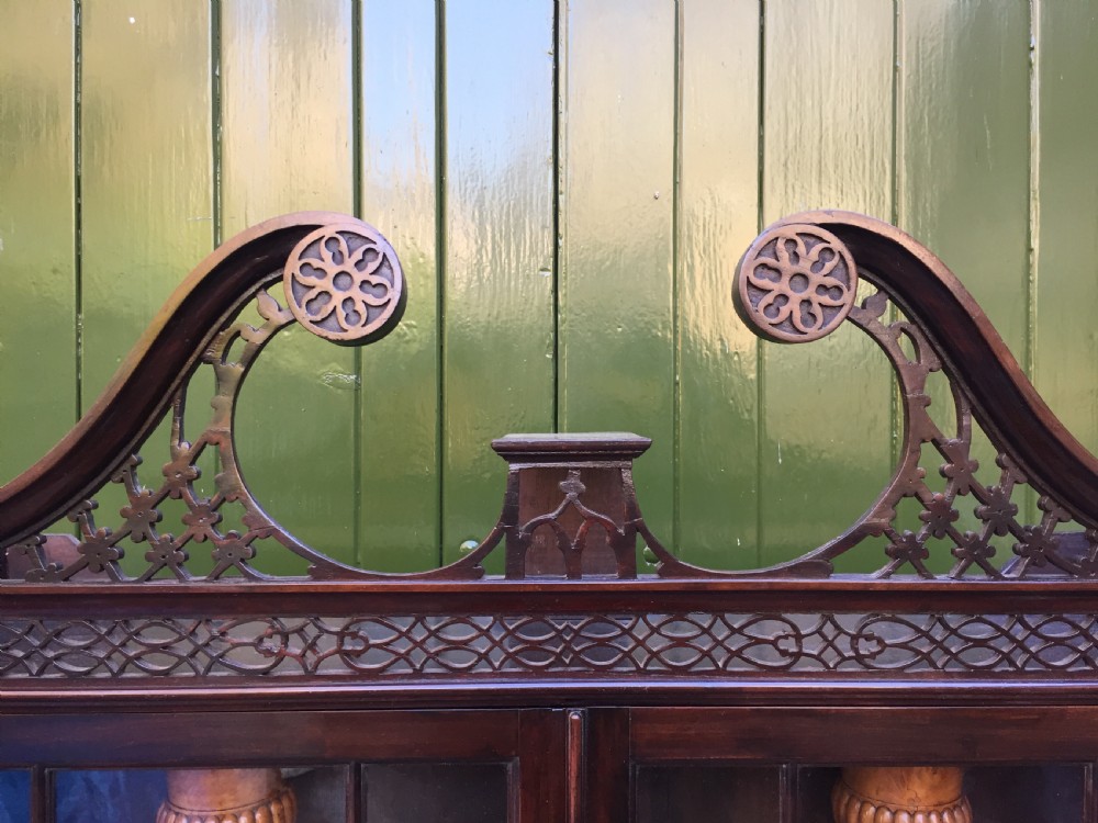 A late 19th-century Chippendale Revival mahogany glazed cabinet on stand featuring a swan-neck pediment, fretwork frieze, astragal glass doors, and turned legs with a lower shelf. View XVI
