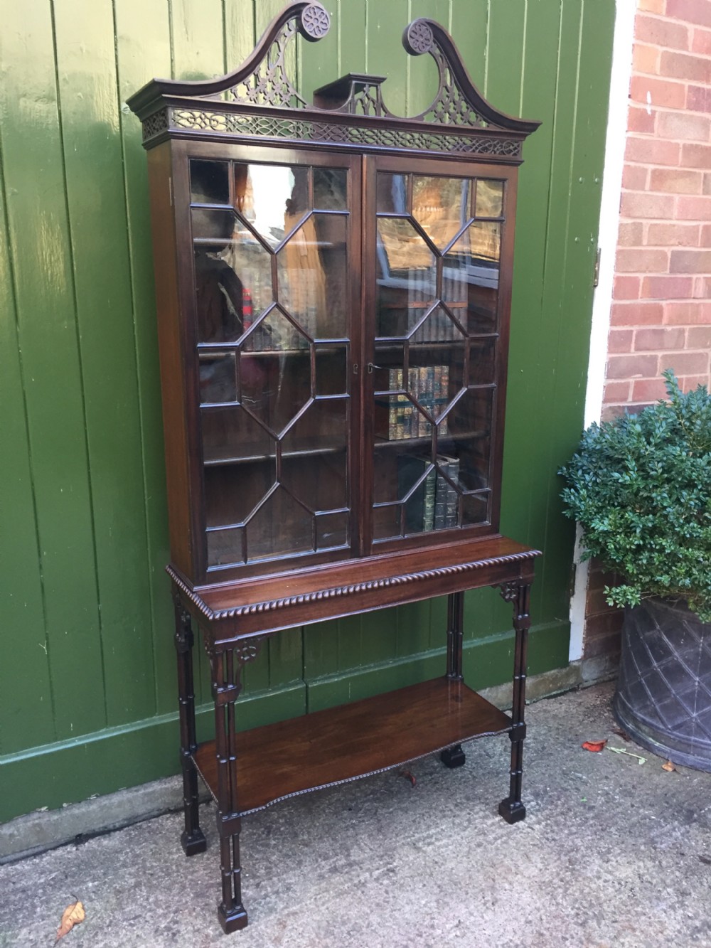 A late 19th-century Chippendale Revival mahogany glazed cabinet on stand featuring a swan-neck pediment, fretwork frieze, astragal glass doors, and turned legs with a lower shelf. View XVIII