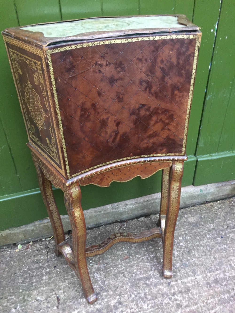 An early twentieth-century French accent table encased in chestnut brown leather with gold leaf tooling, featuring a central cupboard door, open side compartments lined in green damask silk, a small drawer, and cabriole legs. View VII