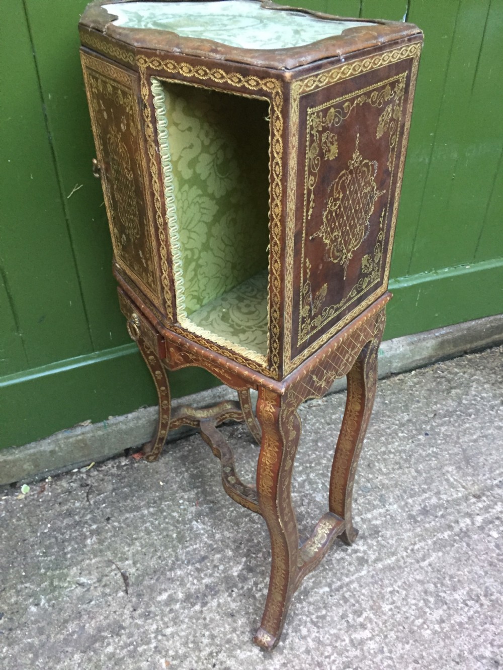 An early twentieth-century French accent table encased in chestnut brown leather with gold leaf tooling, featuring a central cupboard door, open side compartments lined in green damask silk, a small drawer, and cabriole legs. View VIII