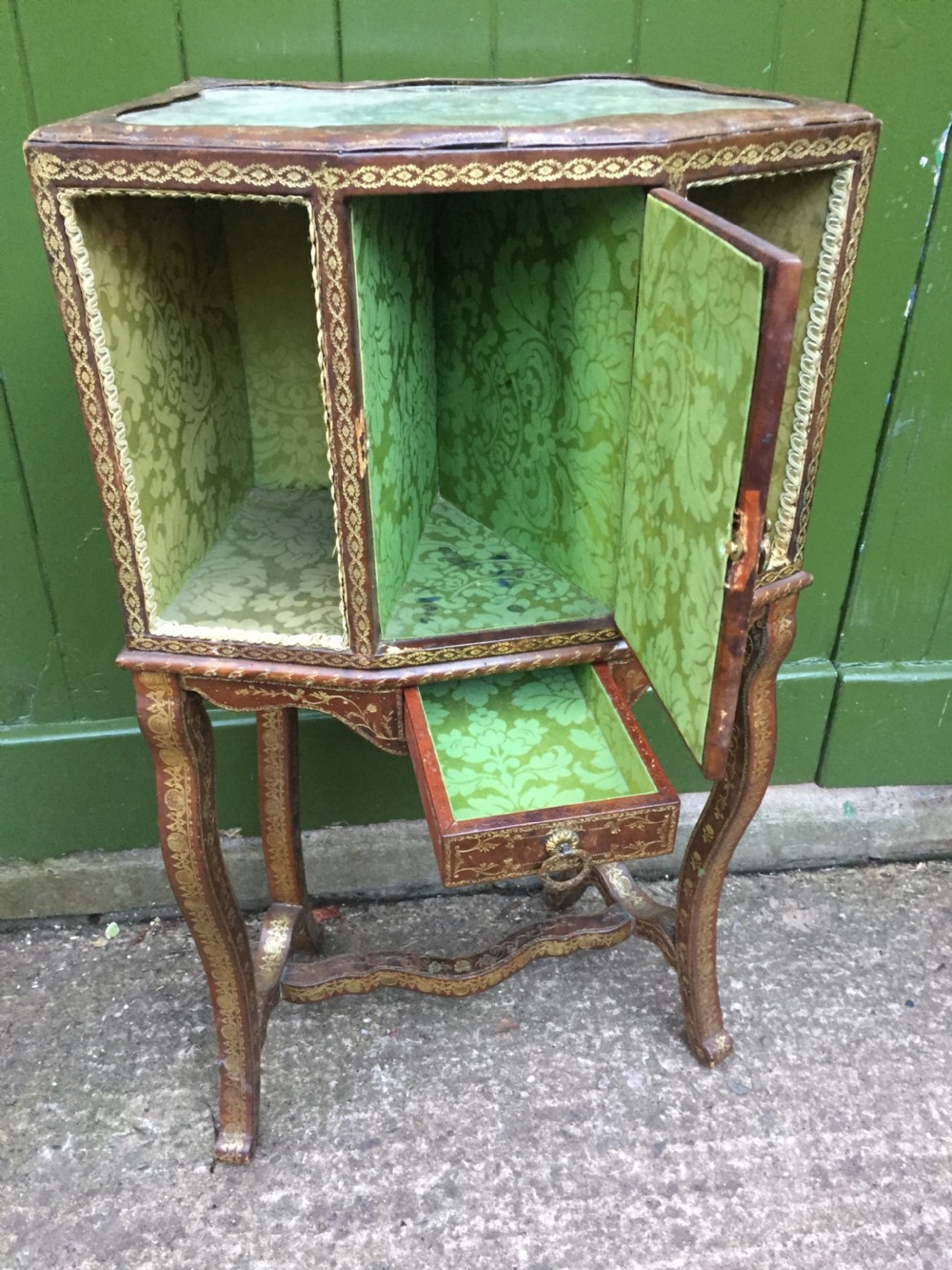An early twentieth-century French accent table encased in chestnut brown leather with gold leaf tooling, featuring a central cupboard door, open side compartments lined in green damask silk, a small drawer, and cabriole legs. View IX