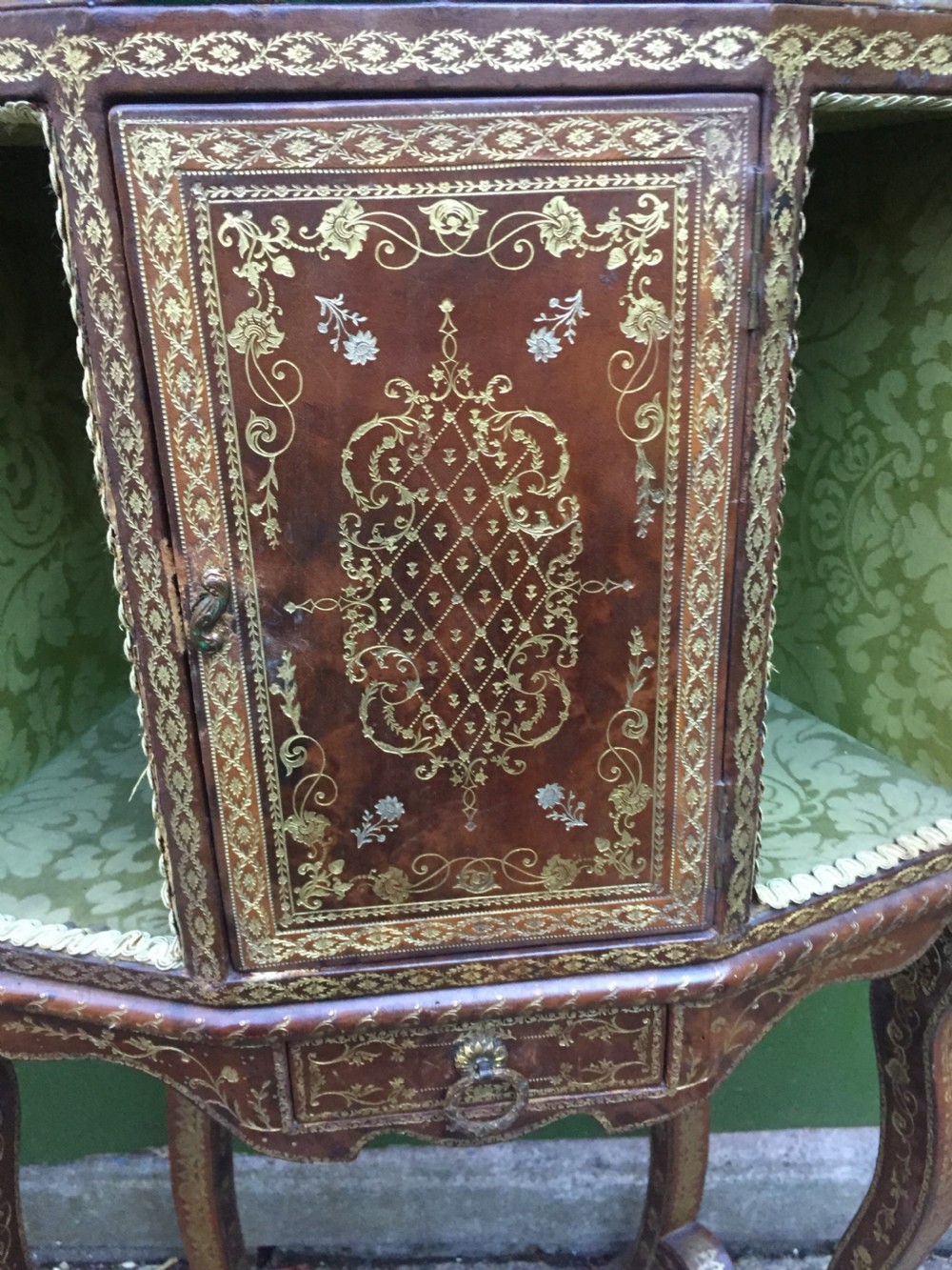 An early twentieth-century French accent table encased in chestnut brown leather with gold leaf tooling, featuring a central cupboard door, open side compartments lined in green damask silk, a small drawer, and cabriole legs. View XI