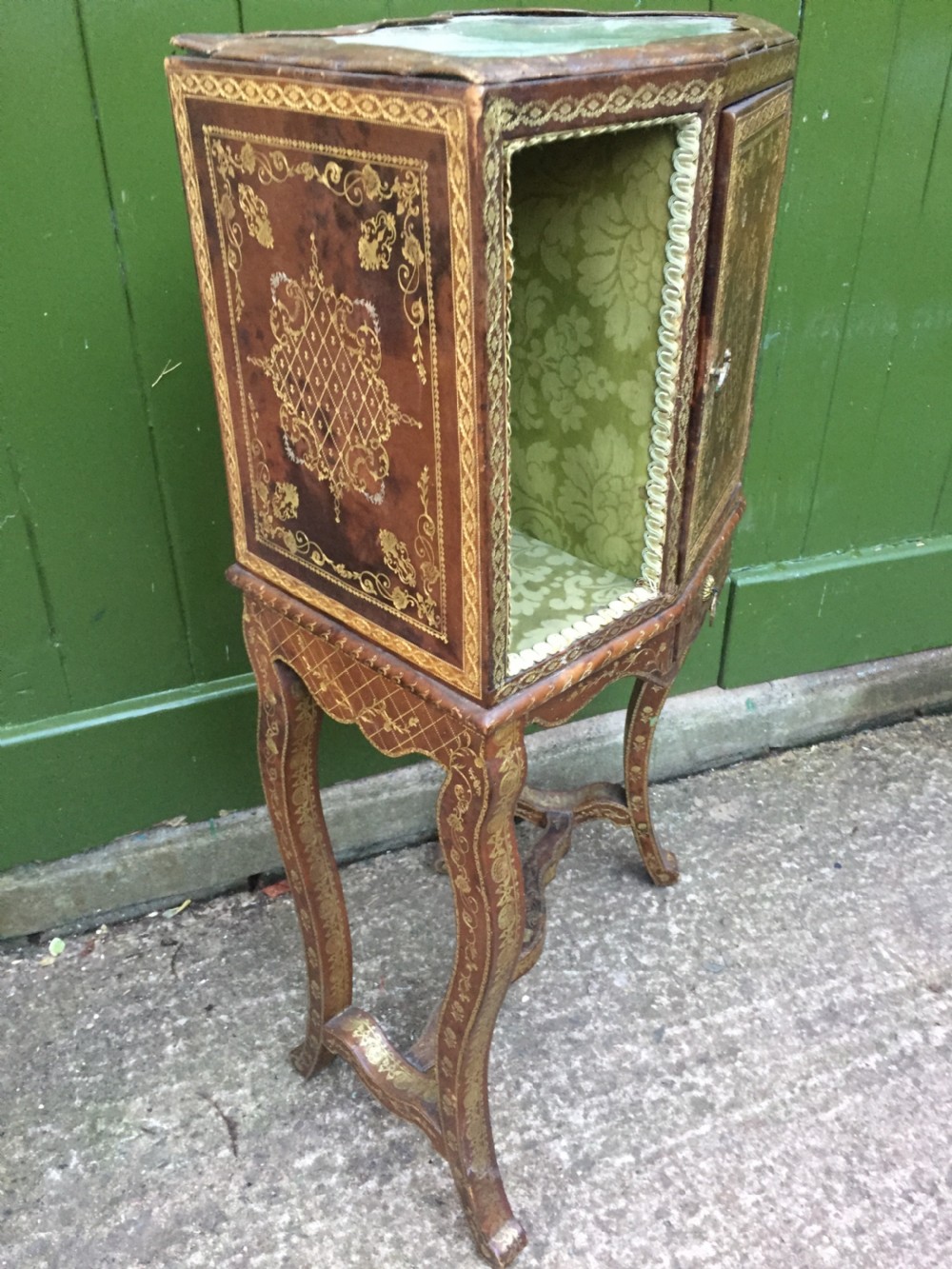 An early twentieth-century French accent table encased in chestnut brown leather with gold leaf tooling, featuring a central cupboard door, open side compartments lined in green damask silk, a small drawer, and cabriole legs. View XV