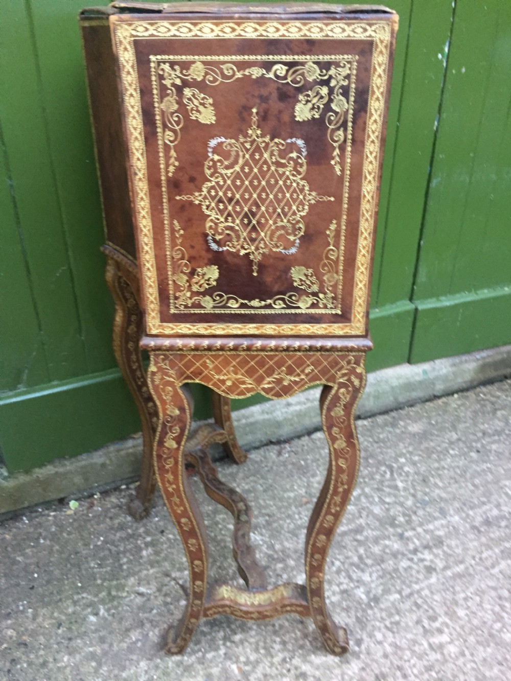 An early twentieth-century French accent table encased in chestnut brown leather with gold leaf tooling, featuring a central cupboard door, open side compartments lined in green damask silk, a small drawer, and cabriole legs. View XVI