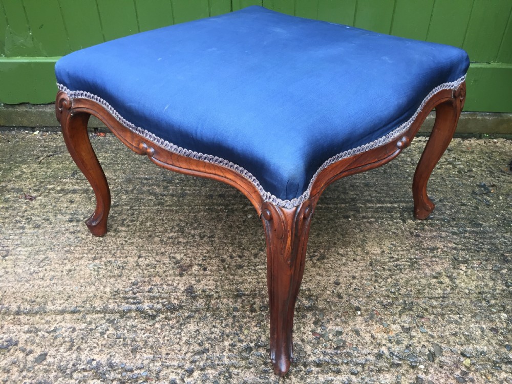 A large mid-nineteenth-century square Victorian stool featuring carved walnut cabriole legs and a blue upholstered top trimmed with gimp braid.