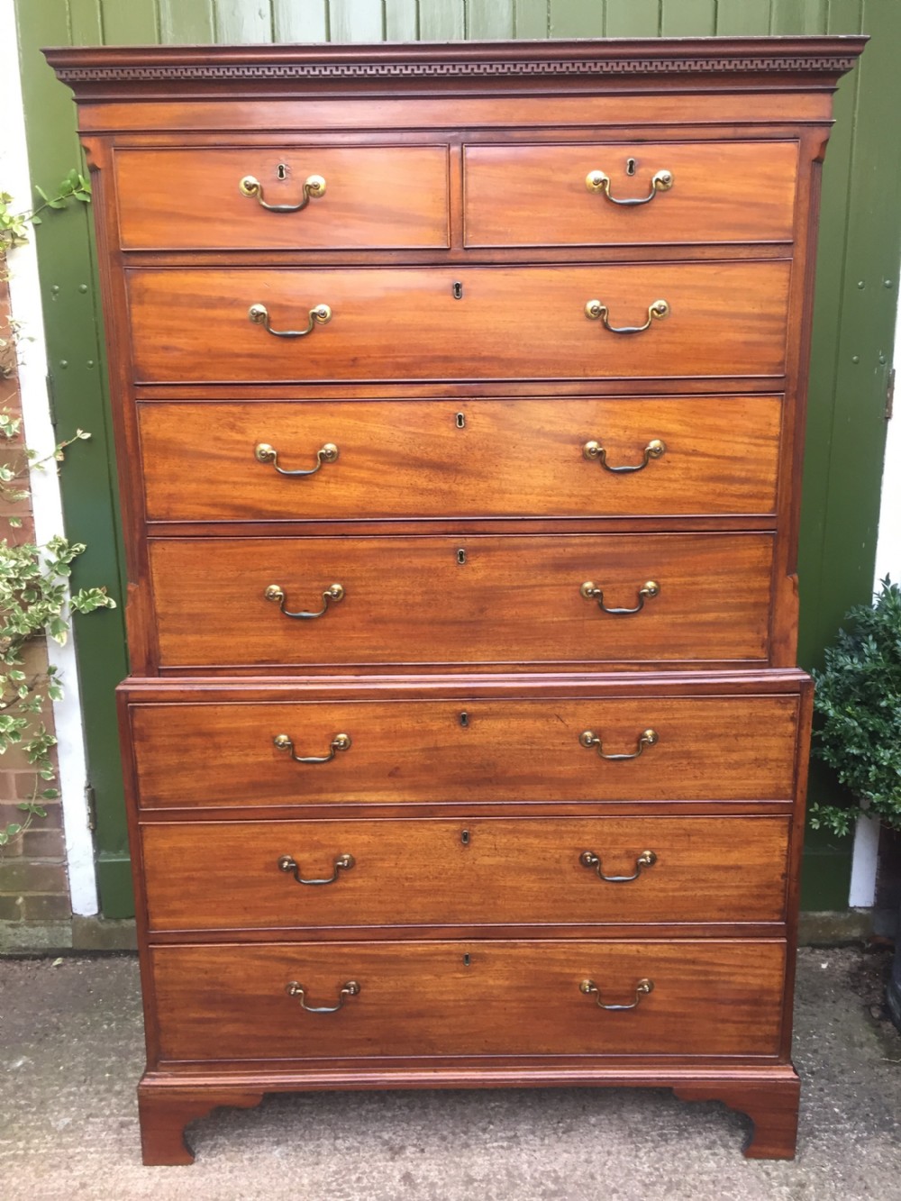 A late eighteenth-century George III mahogany chest-on-chest featuring a dentil moulding cornice, two short over five long graduated drawers with brass swan-neck handles, supported on bracket feet.
