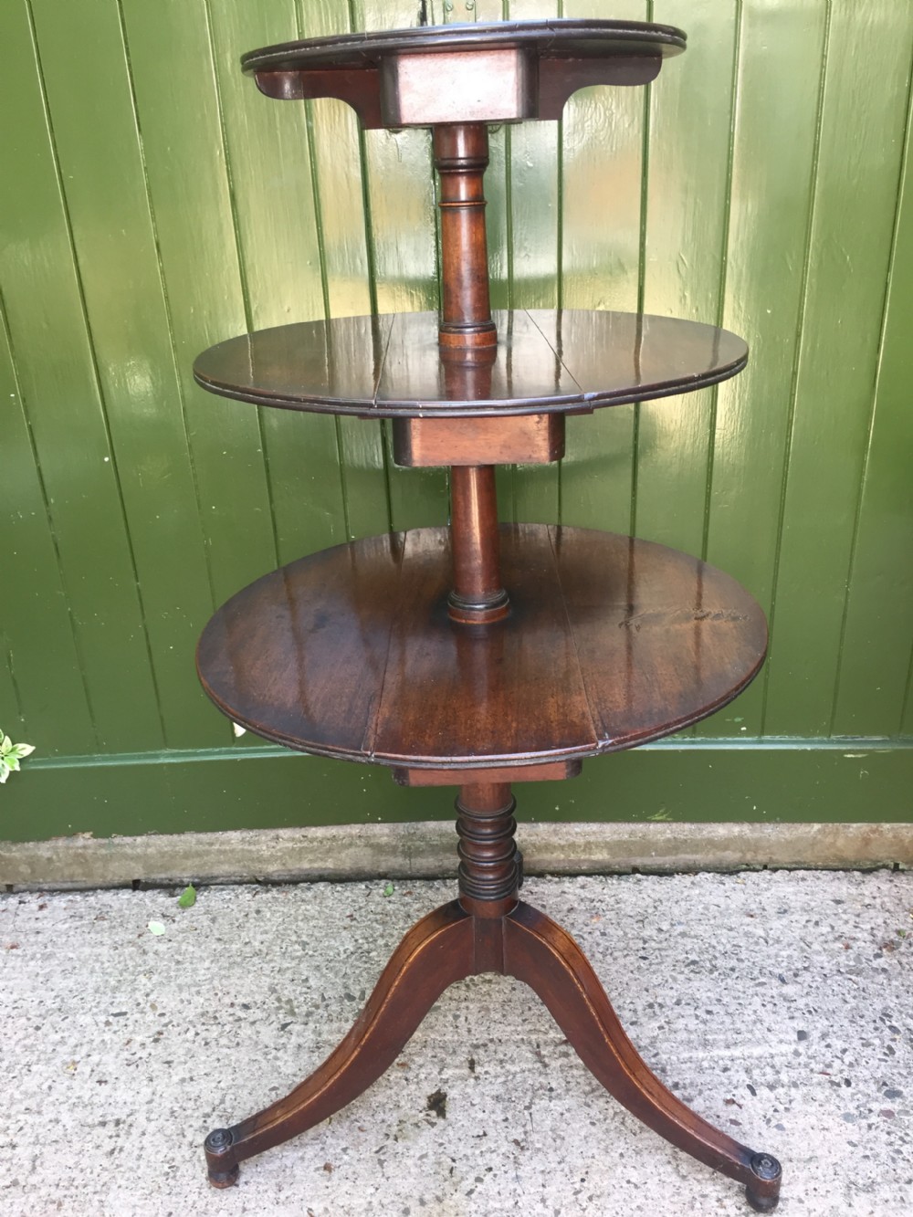 A late 18th-century George III mahogany three-tier circular dumb waiter featuring folding drop-leaf surfaces and a tripod base on castors.