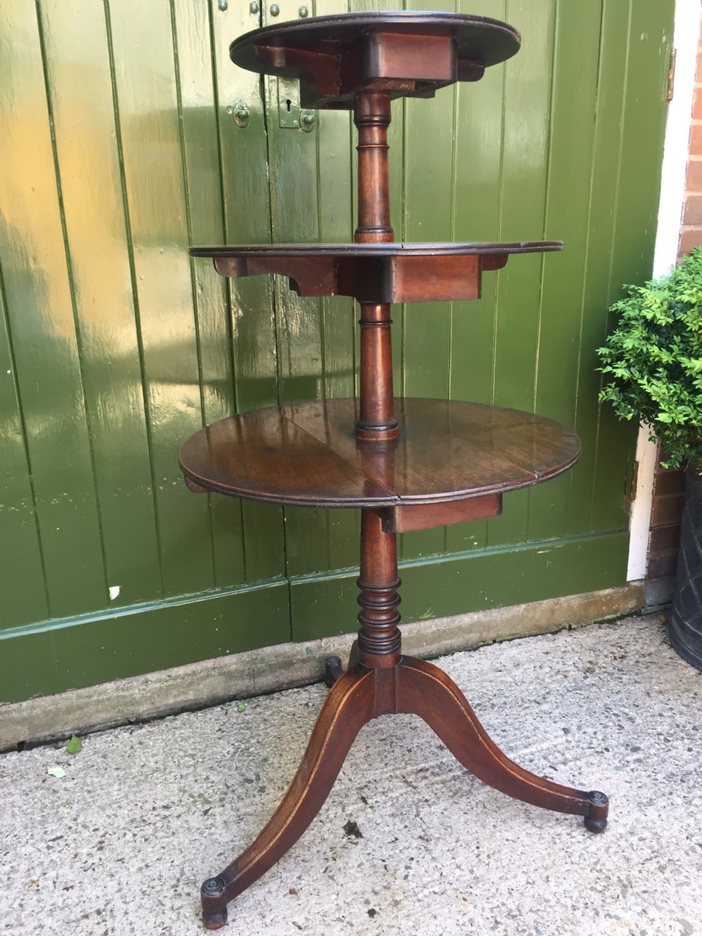 A late 18th-century George III mahogany three-tier circular dumb waiter featuring folding drop-leaf surfaces and a tripod base on castors. View II