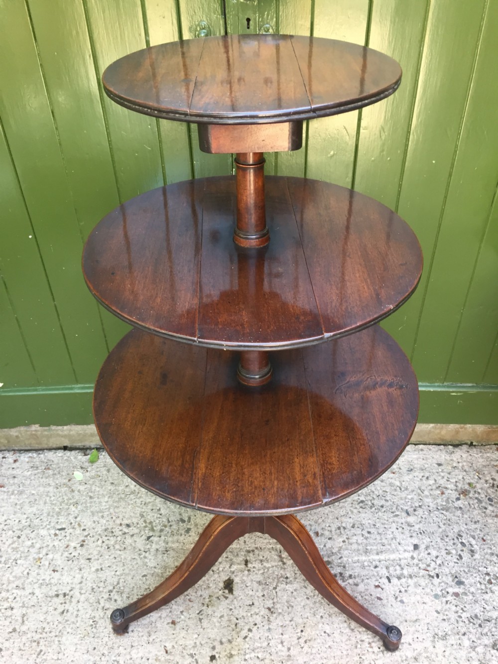 A late 18th-century George III mahogany three-tier circular dumb waiter featuring folding drop-leaf surfaces and a tripod base on castors. View III