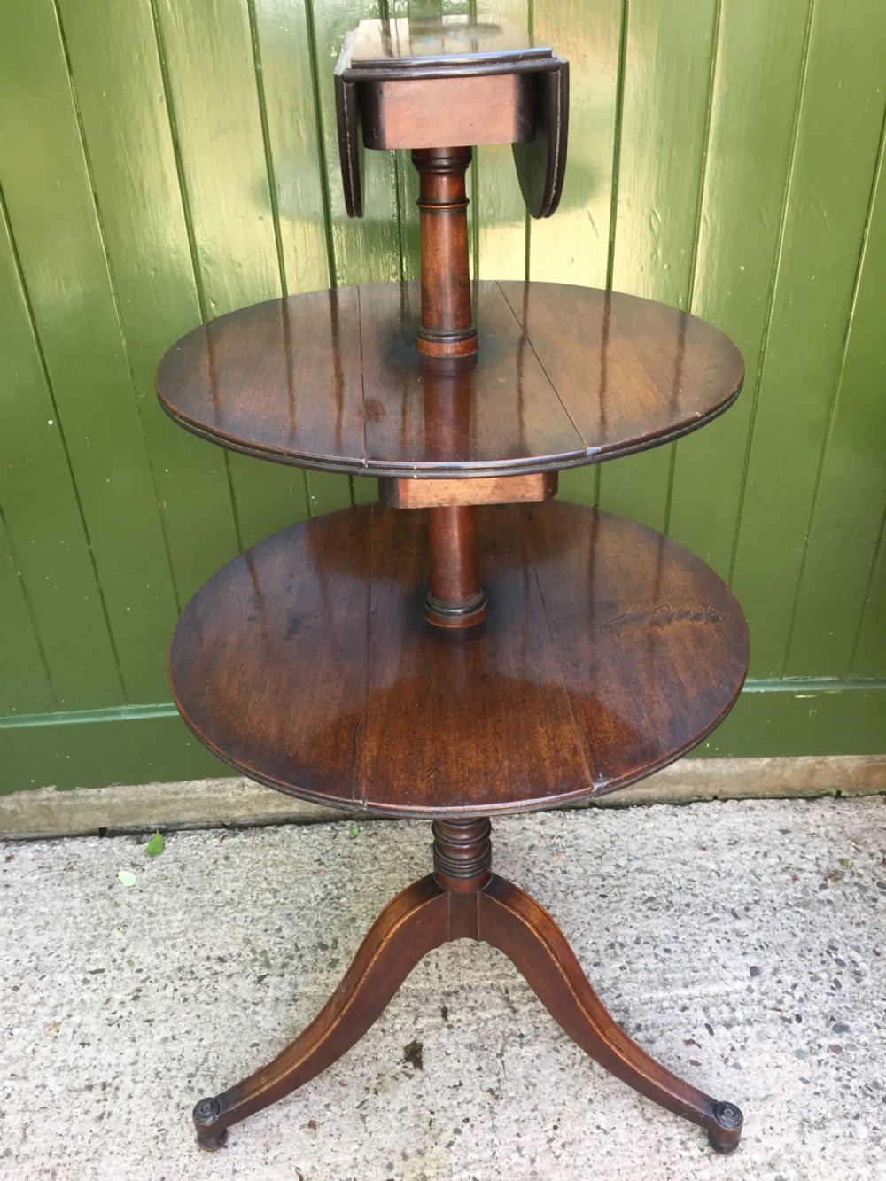 A late 18th-century George III mahogany three-tier circular dumb waiter featuring folding drop-leaf surfaces and a tripod base on castors. View VII