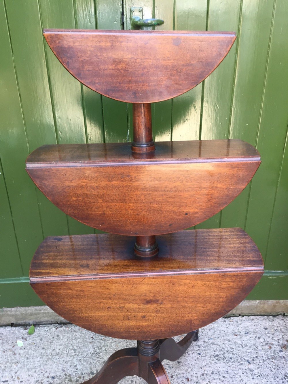A late 18th-century George III mahogany three-tier circular dumb waiter featuring folding drop-leaf surfaces and a tripod base on castors. View X