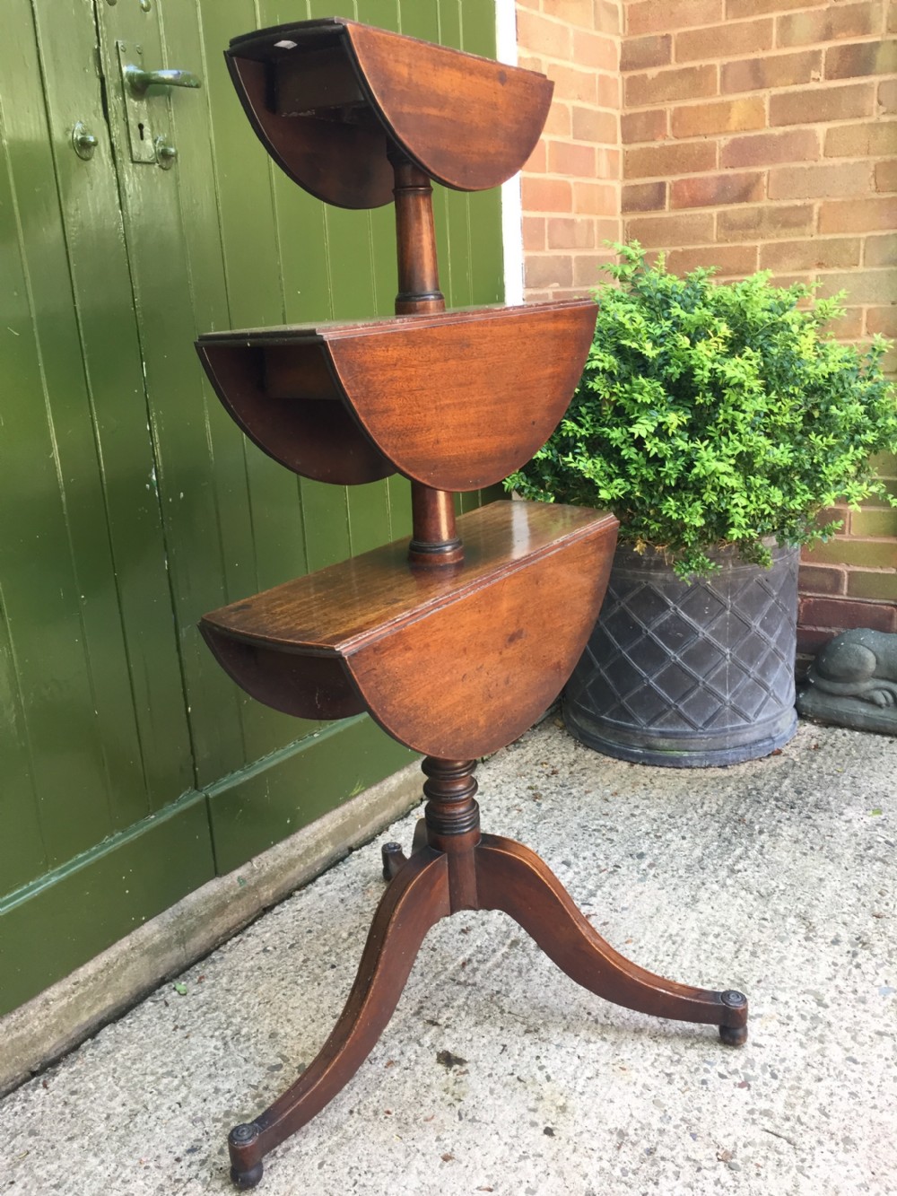 A late 18th-century George III mahogany three-tier circular dumb waiter featuring folding drop-leaf surfaces and a tripod base on castors. View XI
