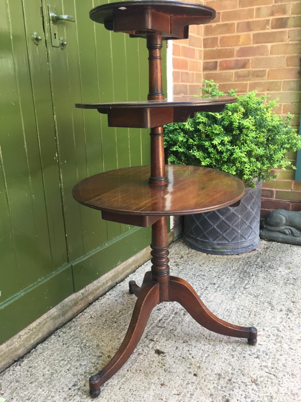 A late 18th-century George III mahogany three-tier circular dumb waiter featuring folding drop-leaf surfaces and a tripod base on castors. View XII