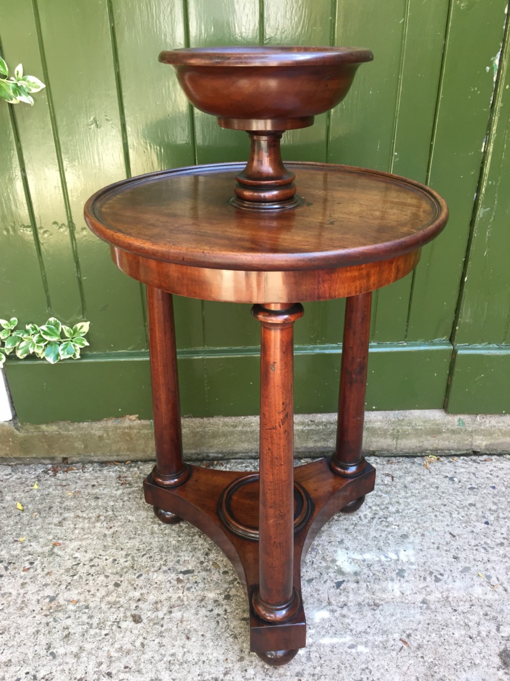 An early 19th-century French circular mahogany vide-poche table featuring a raised turned bowl, three column supports, and a triform base.